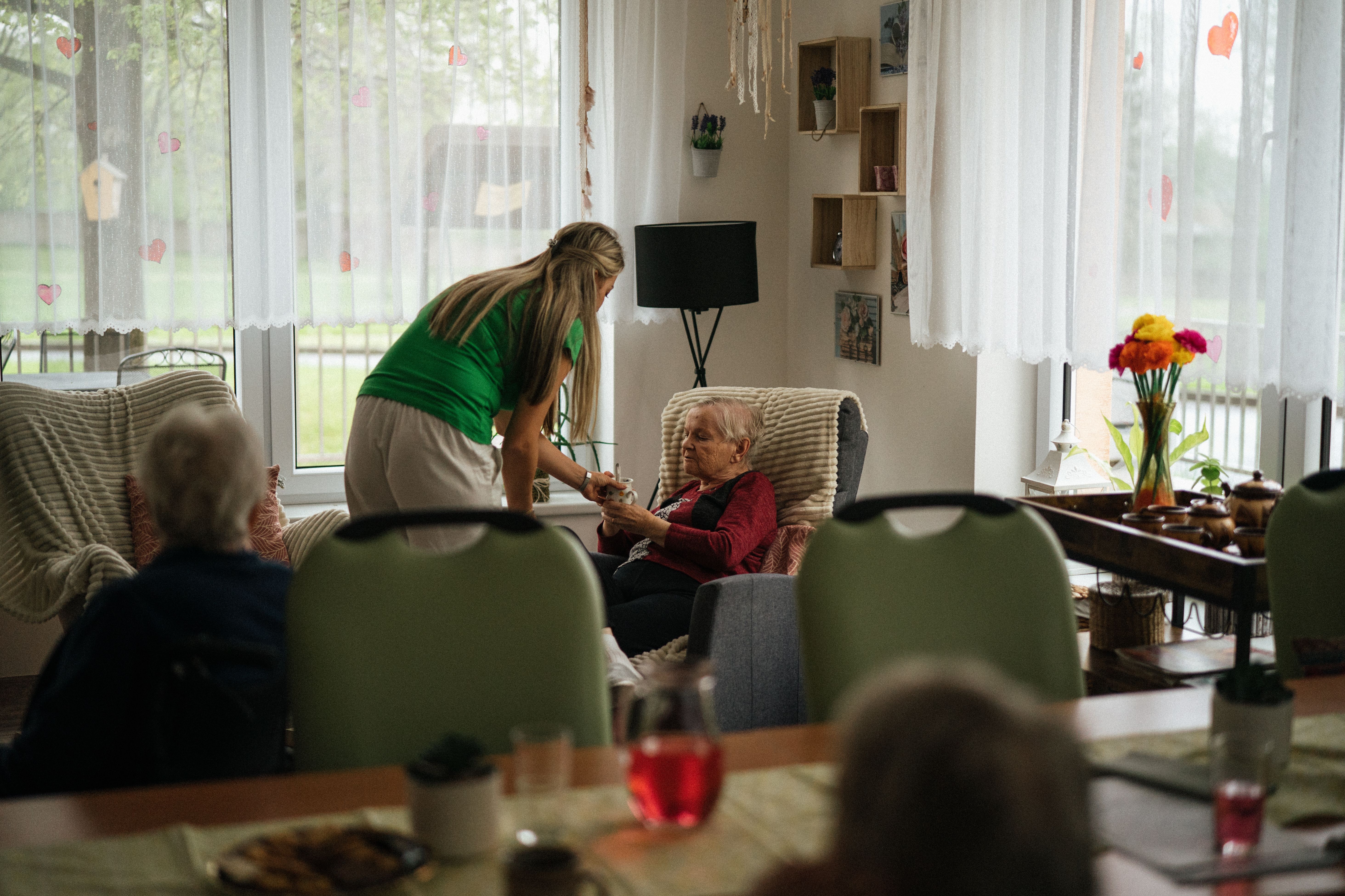 A care worker offering a drink to an elderly resident in a care home common room