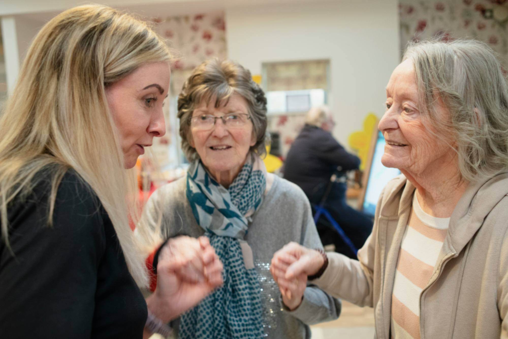 A care worker and an older woman in warm conversation, with another older woman looking on, smiling. Photo by Age Cymru on Unsplash (unsplash.com/@agecymru).